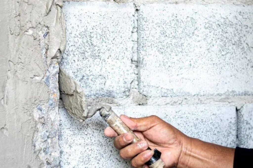 Hand applying fresh mortar to a concrete block wall with a trowel